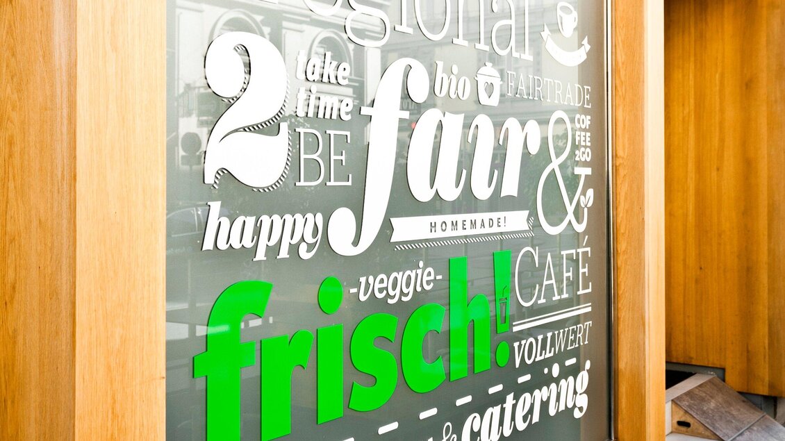 Ein Fenster mit verschiedenen Schriftzügen in Weiß und Grün. Der Text betont frische, vegane und hausgemachte Speisen. | © Mangolds