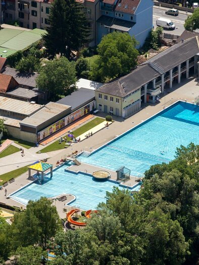 The Margaretenbad with wonderfully blue water and surrounded by green areas. In the background, houses and trees of the city of Graz can be seen. | © Graz Tourismus - Harry Schiffer