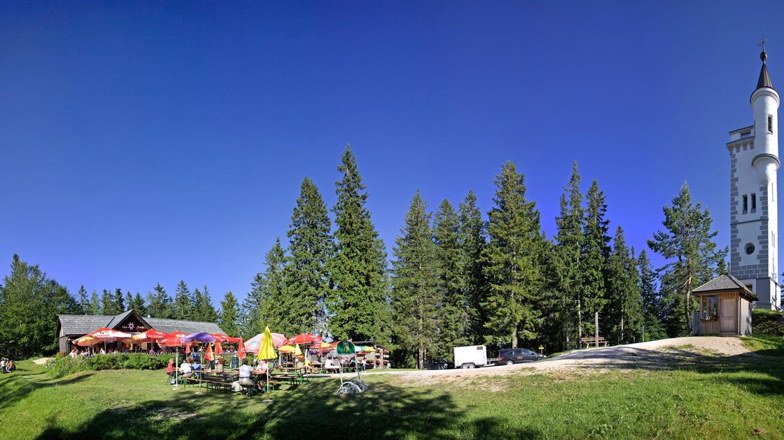 Eine idyllische Landschaft mit einem Restaurant und einer Aussichtsplattform. Umgeben von hohen Bäumen und klarem blauem Himmel. | © TV Hochsteiermark | Fred Lindmoser
