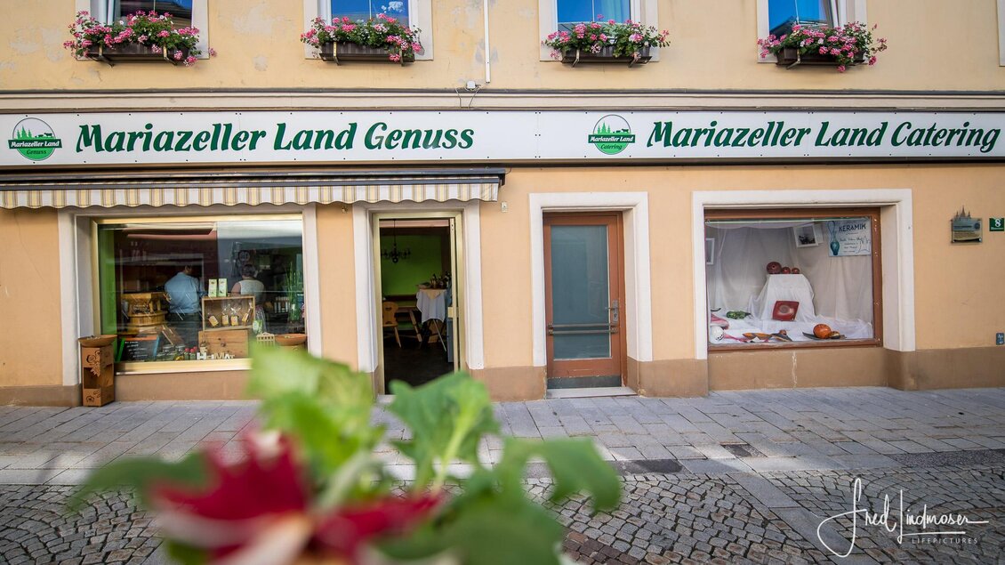Ein Geschäft mit dem Namen "Mariazeller Land Genuss" und "Mariazeller Land Catering" ist zu sehen. Die Fassade ist freundlich gestaltet und mit Blumen dekoriert. | © Fred Lindmoser