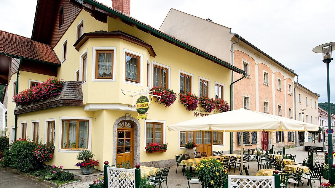 Ein charmantes Restaurant mit gelber Fassade und Blumenschmuck. Draußen stehen gemütliche Tische und Stühle unter Sonnenschirmen. | © Tourismusverband Murau