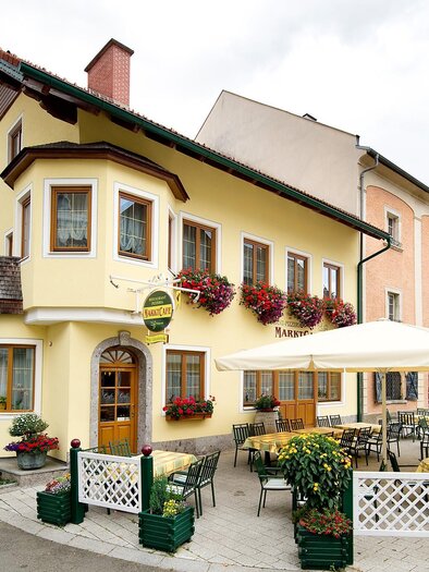 Ein charmantes Restaurant mit gelber Fassade und Blumenschmuck. Draußen stehen gemütliche Tische und Stühle unter Sonnenschirmen. | © Tourismusverband Murau