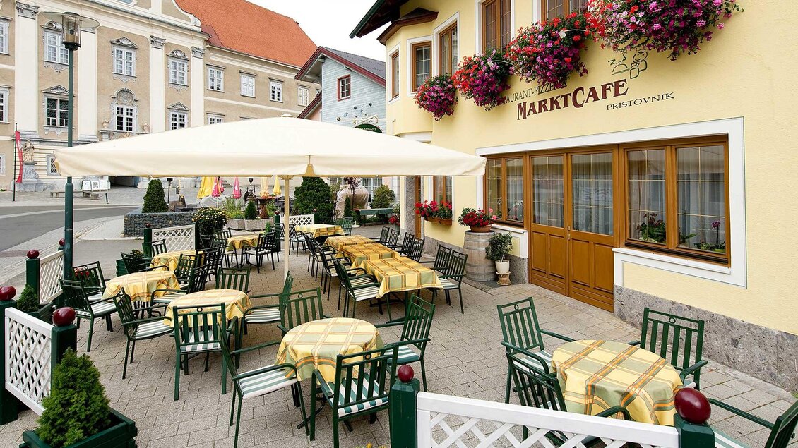 Ein einladendes Café mit einem überdachten Außenbereich. Die Tische sind mit gelben Tischdecken eingedeckt und rundherum blühen Pflanzen. | © Tourismusverband Murau