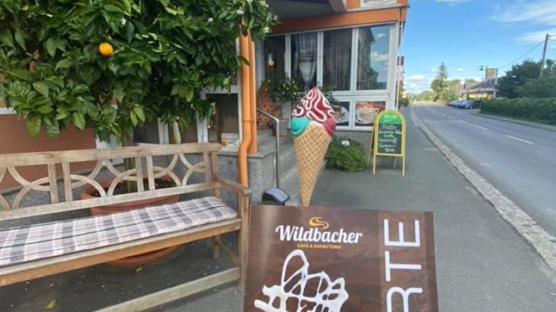 Ein Eissortiment auf einer Karte wird draußen vor einem Eiscafé präsentiert. Im Hintergrund ist ein gemütlicher, lauschiger Ort mit Grünpflanzen zu sehen. | © Marktcafé Wildbacher