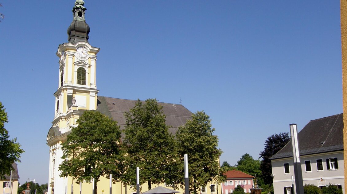 Eine schöne Kirche mit einer beeindruckenden Fassade steht inmitten eines grünen Parks. Der klare blaue Himmel sorgt für eine ruhige Atmosphäre. | © Gemeinde Wies