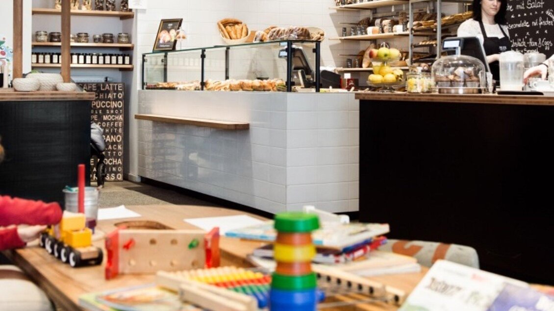 Ein gemütliches Café mit einer Auswahl an Gebäck und Snacks. Im Vordergrund sind Spielsachen und Bücher für Kinder zu sehen. | © Martin Auer