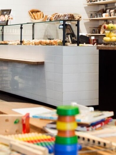 A cozy café with a selection of pastries and snacks. In the foreground, toys and books for children can be seen. | © Martin Auer