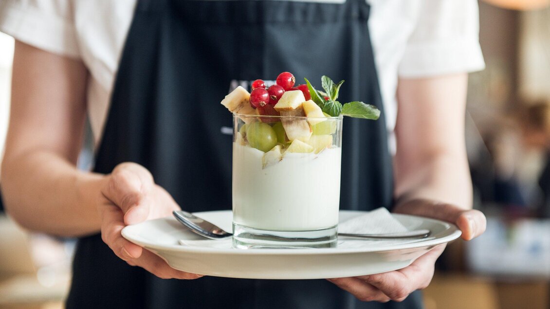 Ein Dessert mit Joghurt und frischen Früchten wird auf einem Teller serviert. Der Teller hat auch einen Löffel und eine Serviette. | © Martin Auer