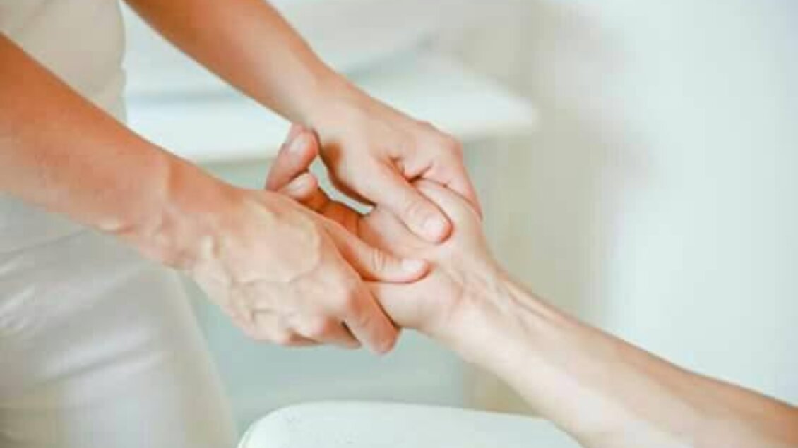 Eine Hand wird sanft massiert. Im Hintergrund ist eine entspannende Umgebung sichtbar.