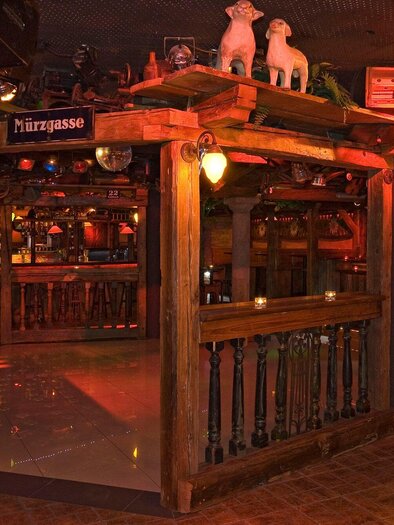 A cozy bar with wooden details and soft lighting. The room has a rustic atmosphere with a view of the counter and seating areas. | © Mausefalle