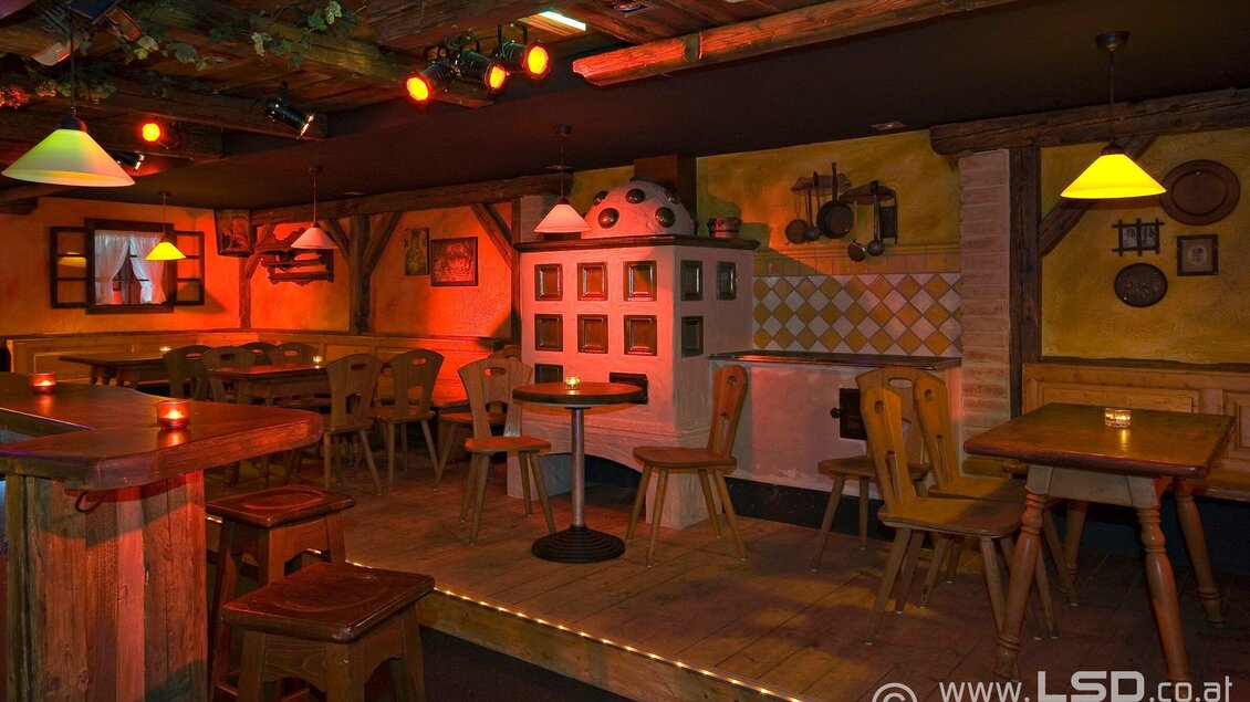 Eine gemütliche Bar mit Holzmöbeln und warmem Licht. An den Wänden befinden sich dekorative Elemente und eine Küche im rustikalen Stil. | © Mausefalle