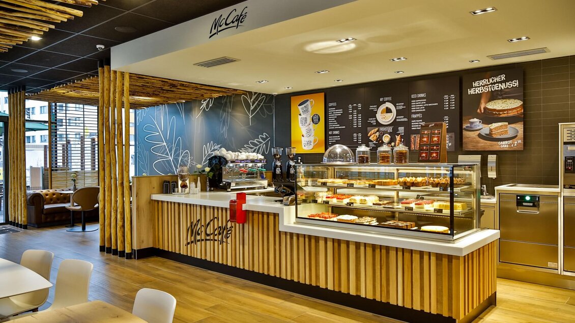 Ein modernes Café mit einer einladenden Theke, die verschiedene Köstlichkeiten präsentiert. Die Einrichtung ist freundlich und hell, mit Holzelementen und angenehmem Licht. | © mcdonalds-oesterreich
