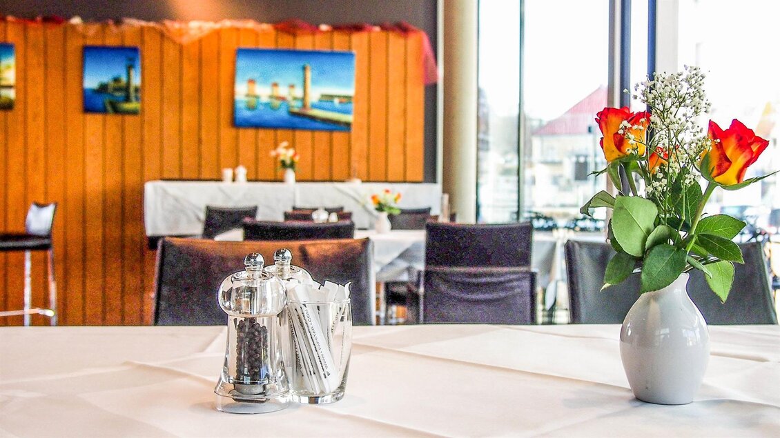 Ein eleganter Restauranttisch mit einem Blumenstrauß aus roten Rosen. Im Hintergrund sind Stühle und einige Bilder an der Wand zu sehen. | © Mediterran - Rathaus Restaurant