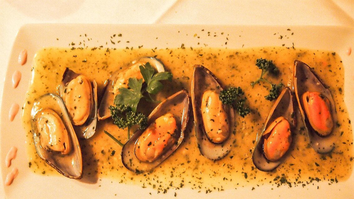 Ein Teller mit frischen Muscheln in einer aromatischen Sauce. Garnierungen aus Petersilie und Kräutern ergänzen das Gericht. | © Mediterran - Rathaus Restaurant