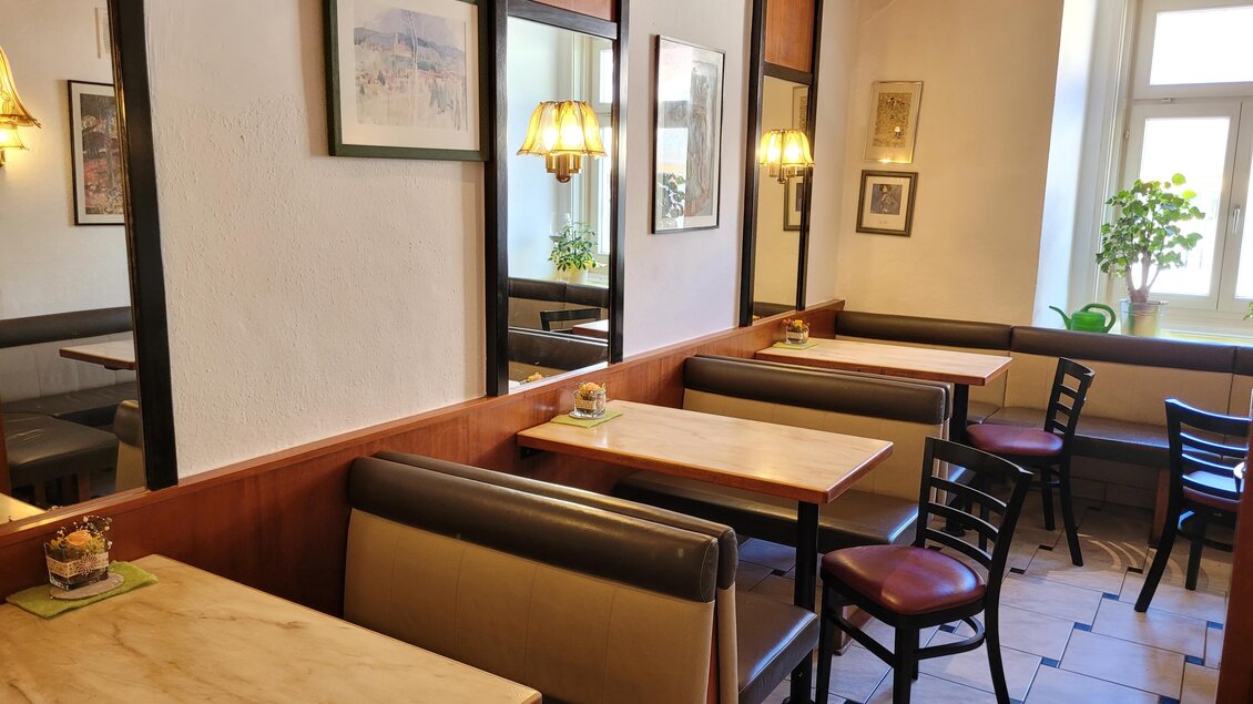 Ein gemütliches Café mit Holztischen und gemütlichen Sitzbänken. Die Wände sind geschmückt mit Bildern und es gibt Pflanzenfenster. | © TV Südsteiermark - Irene Löschnig