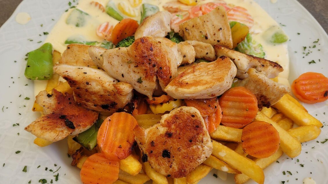 Ein Teller mit gegrilltem Hähnchenfilet, buntem Gemüse und Pommes frites. Die Speise ist mit einer cremigen Sauce garniert. | © TV Südsteiermark - Irene Löschnig