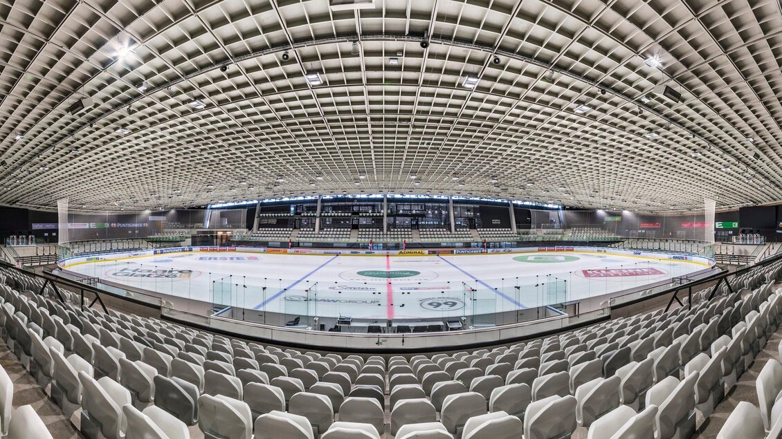 Das Merkur Eisstadion mit einem leeren Eisfeld und zahlreichen Sitzplätzen. Die Decke hat ein modernes Design und die Beleuchtung ist hell. | © MCG - Krug