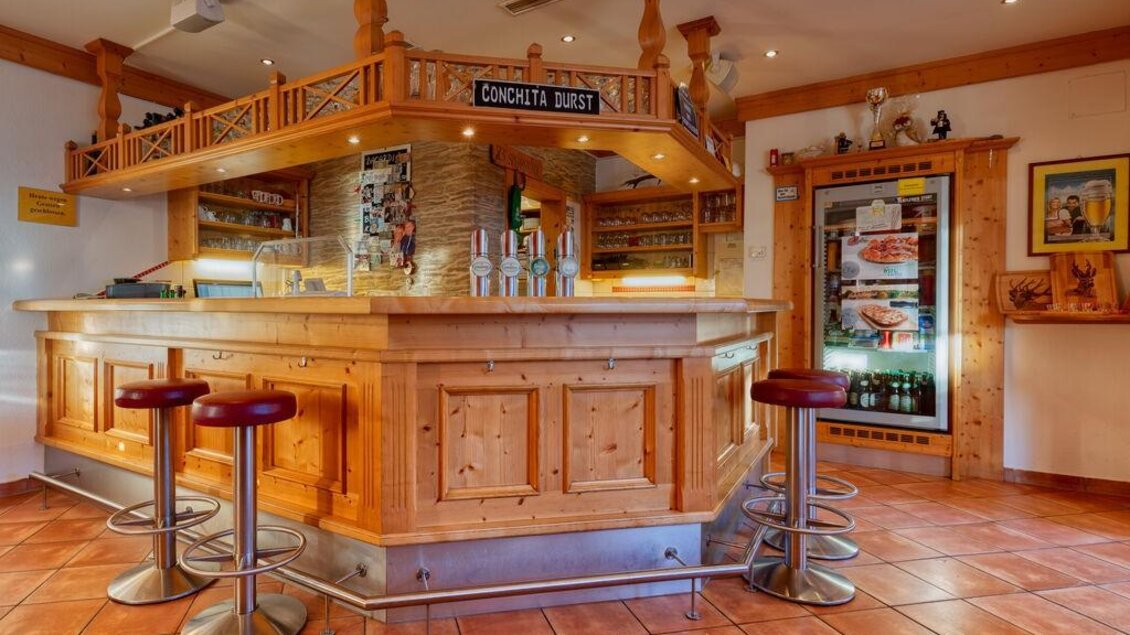 Eine gemütliche Bar mit einem Holztresen und modernen Barhockern. Im Hintergrund sind Getränke und dekorative Elemente sichtbar. | © Michis Bierstubn