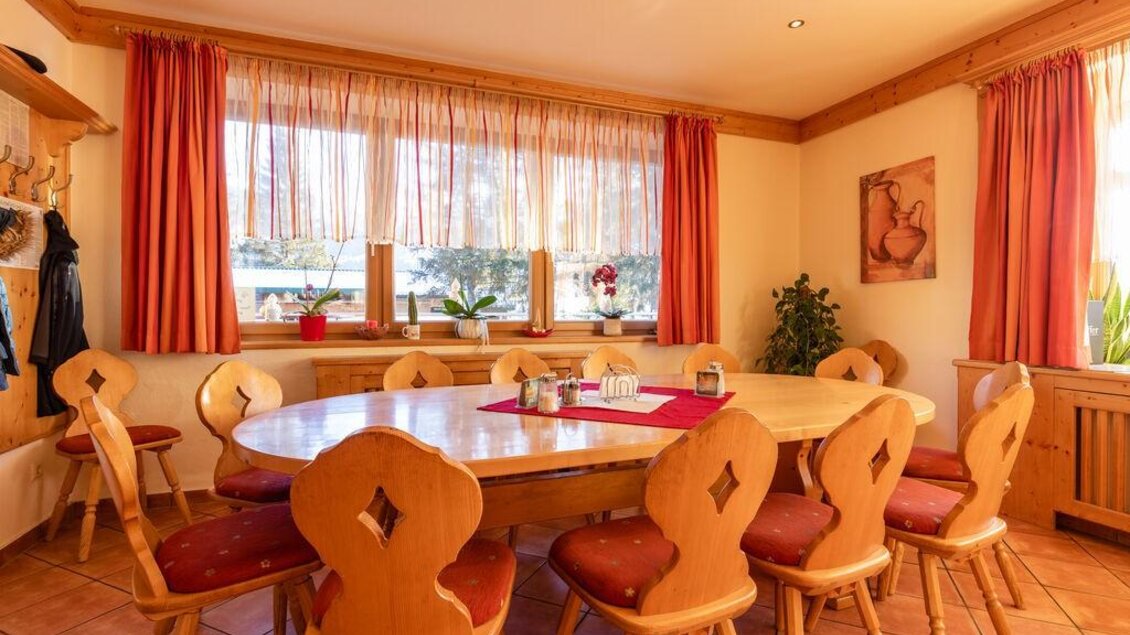 Ein einladender Essbereich mit einem runden Holztisch und gemütlichen Stühlen. Große Fenster lassen viel Licht herein und der Raum hat eine warme Atmosphäre. | © Michis Bierstubn