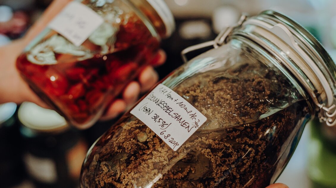 Zwei Gläser mit eingelegten Lebensmitteln, eines mit roten Früchten und das andere mit getrockneten Kräutern. Beide Gläser sind beschriftet und werden von einer Person gehalten. | © GenussReich