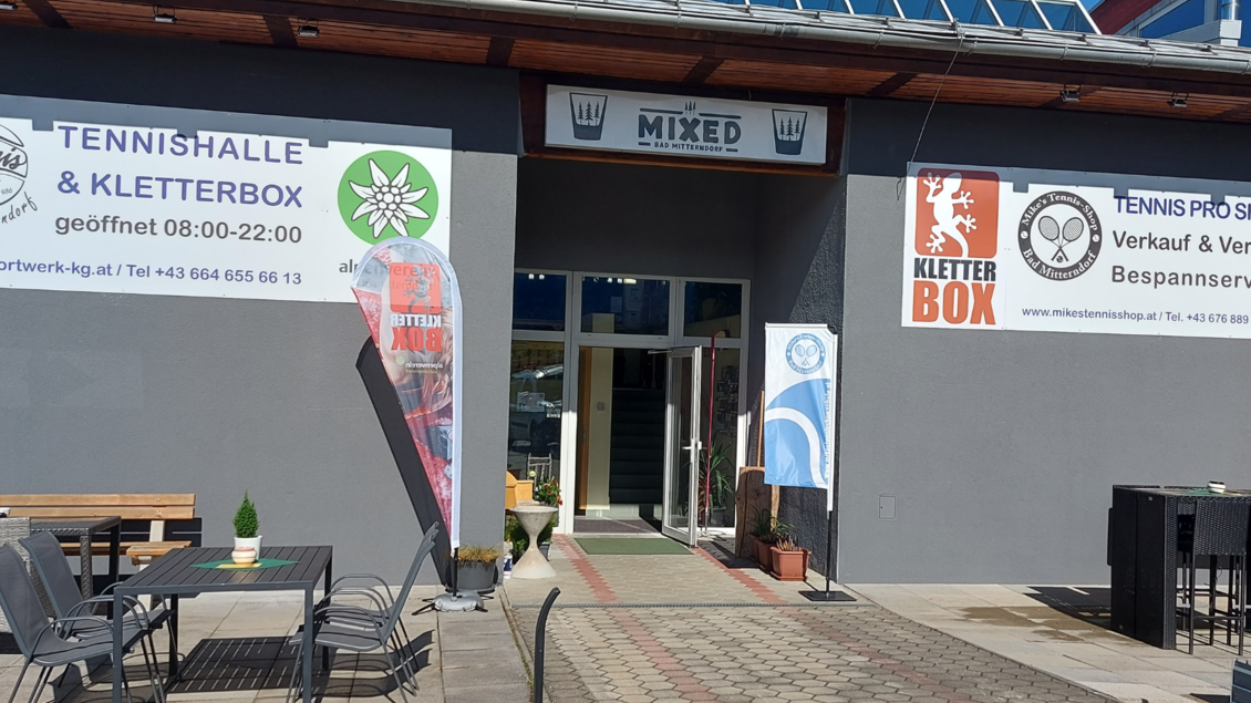 Ein Eingangsbereich eines Sportzentrums mit Schildern für Tennis und Klettern. Vor dem Gebäude befinden sich einige Tische und Stühle. | © Mike Krug
