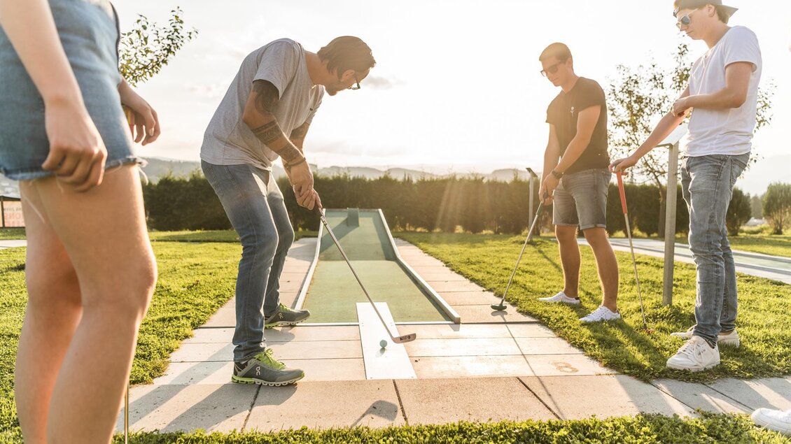 Eine Gruppe von vier Personen spielt Minigolf auf einer grünen Wiese. Die Sonne scheint und es herrscht eine entspannte Atmosphäre. | © Lipizzanerheimat_Die Abbilderei