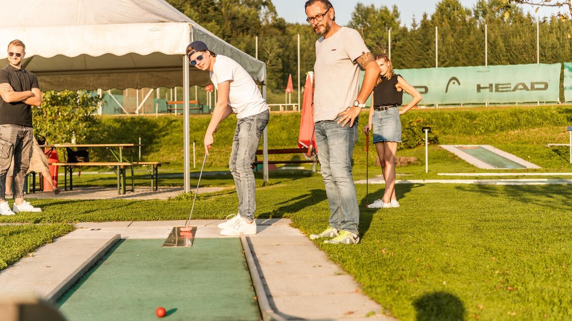 Eine Gruppe von Menschen spielt Minigolf in einem schönen Außenbereich. Im Hintergrund sind grüne Rasenflächen und ein Zelt zu sehen. | © Lipizzanerheimat_Die Abbilderei