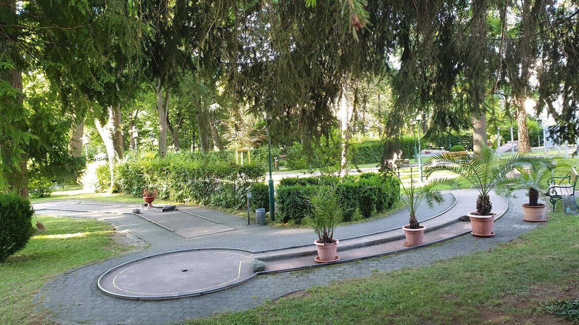 Ein gepflegter Park mit einem geschwungenen Weg. Einige Pflanzen in Tontöpfen schmücken die Umgebung. | © Minigolfanlage Knittelfeld