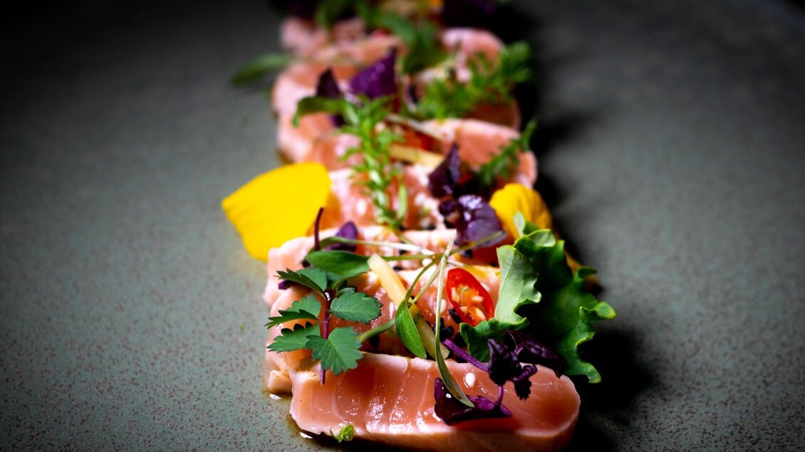 Dünn geschnittener Fisch mit Kräutern, Blüten und Sesam kunstvoll angerichtet. | © Miss Cho - aiola
