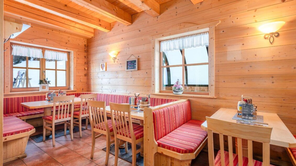 Ein gemütliches Restaurant mit Holzvertäfelung und roten Stoffsofas. Die Tische sind ordentlich gedeckt und die Fenster bieten einen Blick nach draußen. | © Mitterhausalm | Alpine Genusswelten