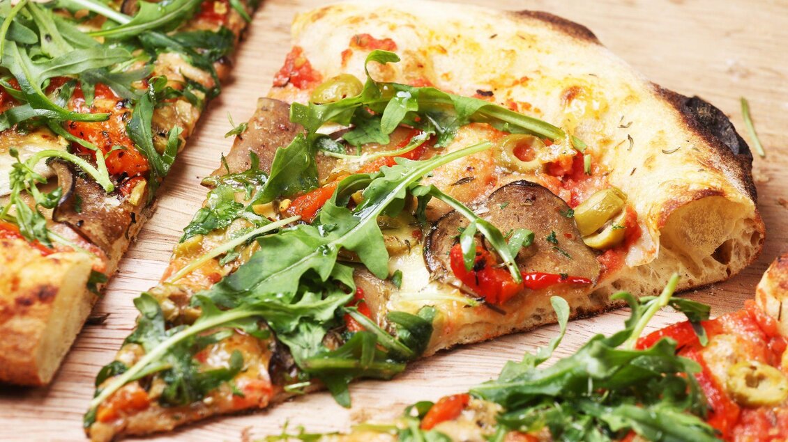 Ein Stück Pizza mit frischem Rucola, roten Paprika und Oliven. Der Teig ist knusprig und goldbraun. | © Pixabay