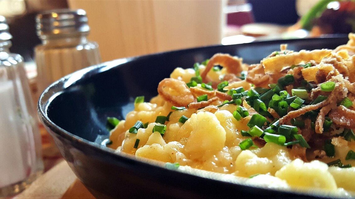 Ein Teller mit cremigen Käsespätzle, garniert mit frischem Schnittlauch und knusprigen Zwiebelringen. Im Hintergrund sind Salz- und Pfefferstreuer zu sehen. | © Pixabay