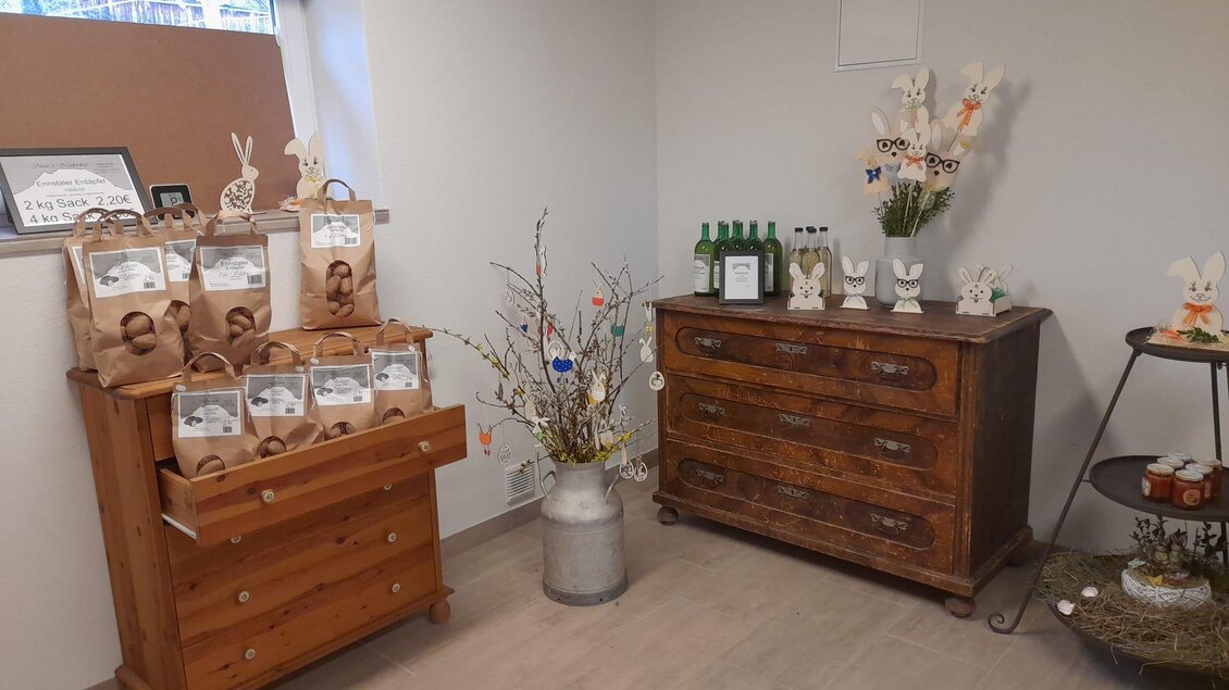 Ein gemütlicher Raum mit einer Holzkommode und einem Tisch, der dekoriert ist. Auf der Kommode stehen Geschenktüten und Flaschen, umgeben von dekorativen Elementen. | © Moar in Niederdorf