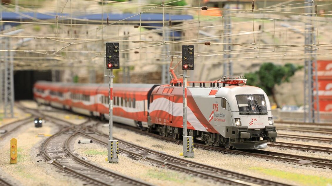 Ein Modellzug fährt durch eine detailreiche Eisenbahnanlage. Die Szenerie zeigt Gleise, Signale und eine beeindruckende Tunnelkulisse. | © Modelleisenbahn Knittelfeld