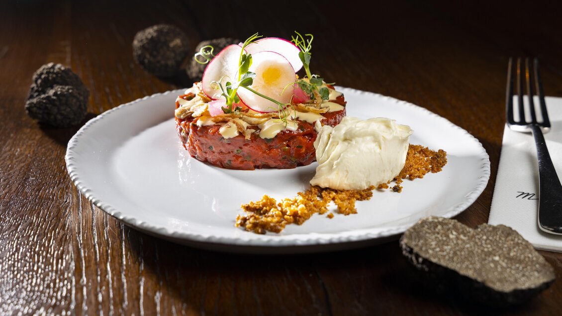 Rindstatar mit Radieschenscheiben, Sauce, knusprigen Zwiebeln und Trüffelcreme auf weißem Teller angerichtet. | © Graz Tourismus - Werner Krug