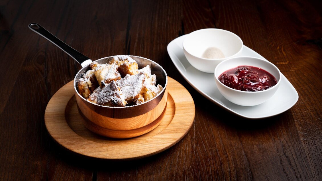 Ein leckerer Dessertteller mit gebackenen Stückchen, bestreut mit Puderzucker, serviert in einer kleinen Pfanne. Dazu gibt es Vanilleeis und eine Schale mit Fruchtsoße. | © Mohrenwirt