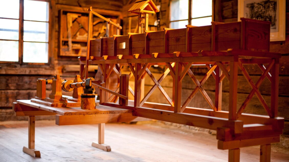 Ein Holzwerkzeug auf einem Tisch in einem rustikalen Raum. Im Hintergrund sind Fenster und weitere Holzstrukturen sichtbar. | © Holzwelt Murau