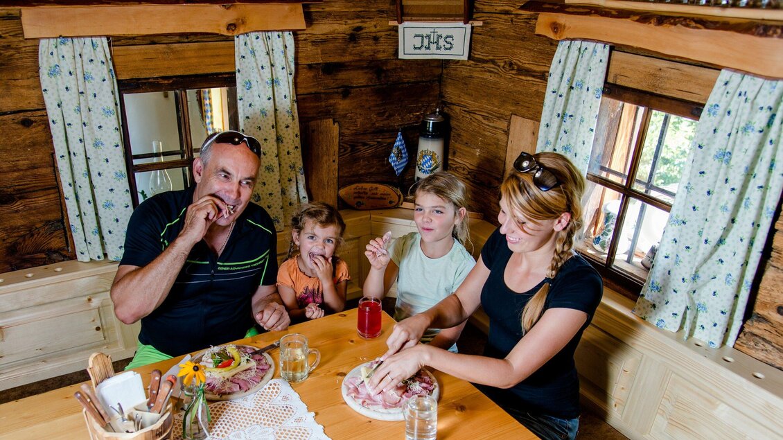 Eine Familie sitzt am Tisch in einer gemütlichen Holzhütte und genießt ihr Essen. Es gibt lachende Gesichter und fröhliche Atmosphäre. | © TV Region Graz - Mias Photoart