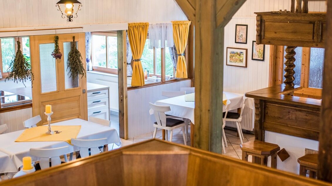 Ein gemütlicher Innenraum mit hellen Tischen und Stühlen. Große Fenster lassen viel Licht herein, und dekorative Fensterbehänge sorgen für eine einladende Atmosphäre. | © Serschenhof