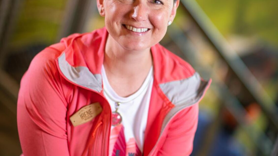 Eine lächelnde Frau sitzt in einem Innenraum. Sie trägt eine rosa Jacke und wirkt freundlich und einladend. | © Mountain Shop Schladming