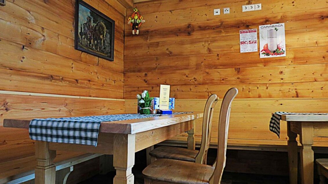 Ein gemütlicher Gastraum mit Holzwänden und traditionellen Möbeln. Auf den Tischen liegen karierten Tischdecken, und es gibt eine kleine Pflanze auf dem Tisch. | © Mur Heuriger