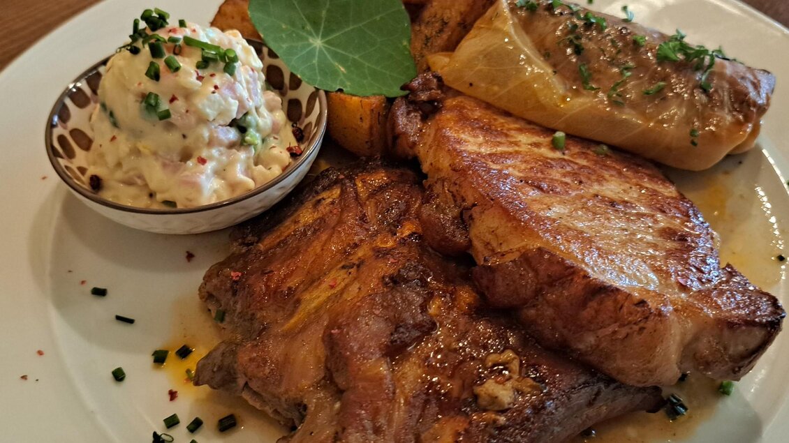 Ein rustikeller Teller mit gegrilltem Fleisch, gebratenen Kartoffeln und einer Portion Salat. Dazu gibt es ein gefülltes Gemüse und frische Kräuter. | © Johannes Ulrich