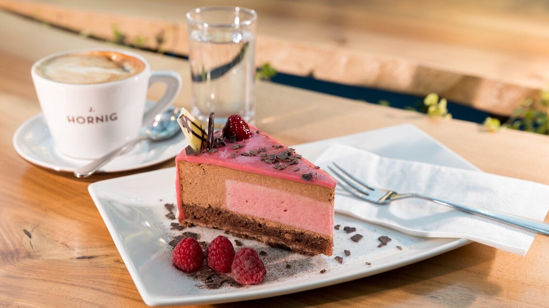 Ein Stück köstliche Torte mit Himbeeren und Schokoladendekor. Daneben steht eine Tasse Kaffee und ein Glas Wasser. | © Graz Tourismus - Harry Schiffer