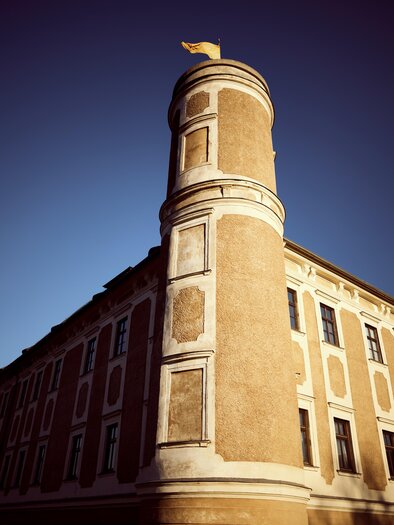 A historic building with a round tower. The tower has a flag and is surrounded by blue sky. | © Armin Walcher