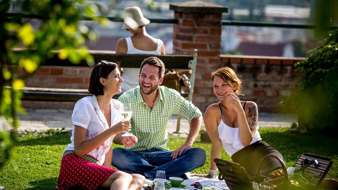 Drei Personen beim Picknick auf einer Wiese im Garten des Volkskundemuseums Graz. | © Graz Tourismus-Tom Lamm