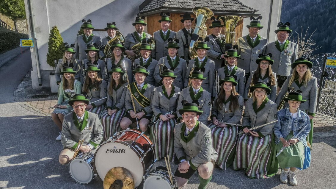 Eine Blaskapelle steht in traditionellen Trachten vor einem Gebäude. Alle Mitglieder tragen grüne Hüte und lächeln in die Kamera. | © Heinz & Melitta Holzmüller