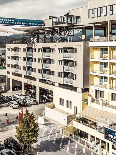 A modern hotel with an airplane model on the roof. The surroundings are urban with parking spaces and trees. | © Novapark - Ulrike Rauch