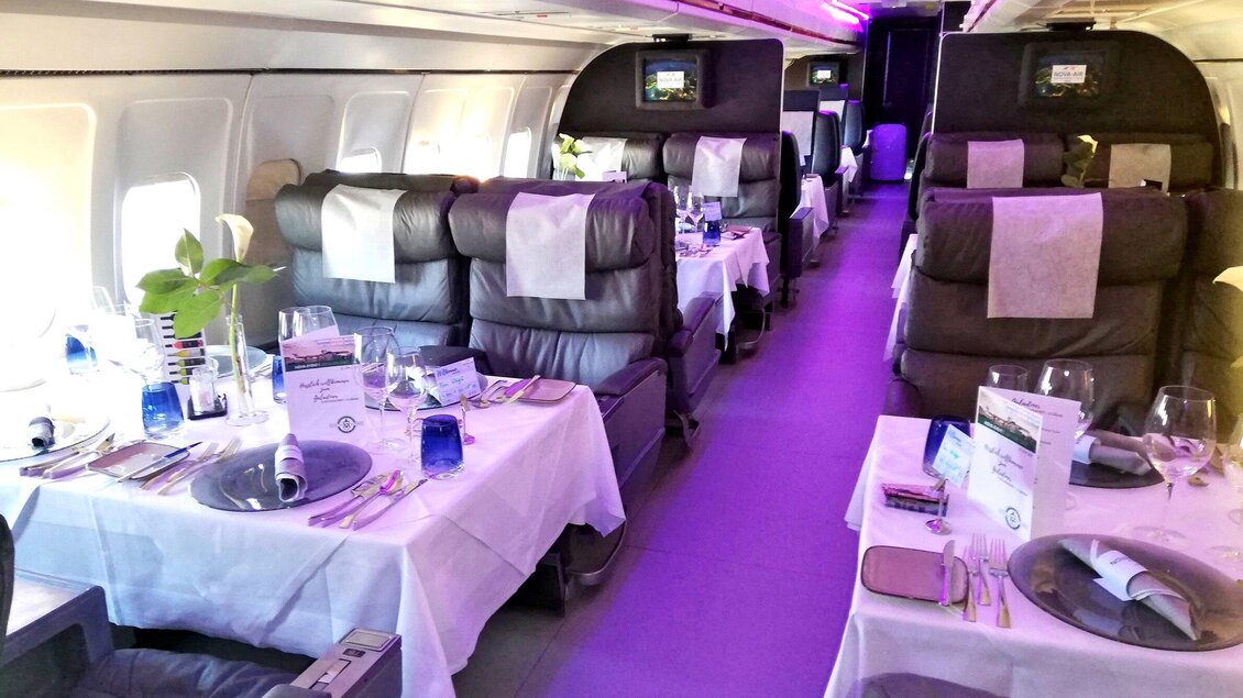 Ein eleganter Innenraum eines Flugzeugs mit stilvoll gedeckten Tischen. Der Raum ist gut beleuchtet und bietet komfortable Sitzplätze. | © NOVAPARK