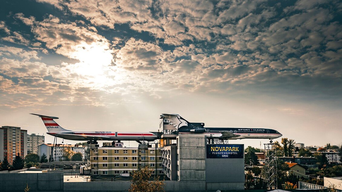 Ein Flugzeug steht auf einem Gebäude mit einer dramatischen Wolkenlandschaft im Hintergrund. Die Szenerie vermittelt einen modernen und ungewöhnlichen Eindruck. | © NOVAPARK - Ulrike Rauch