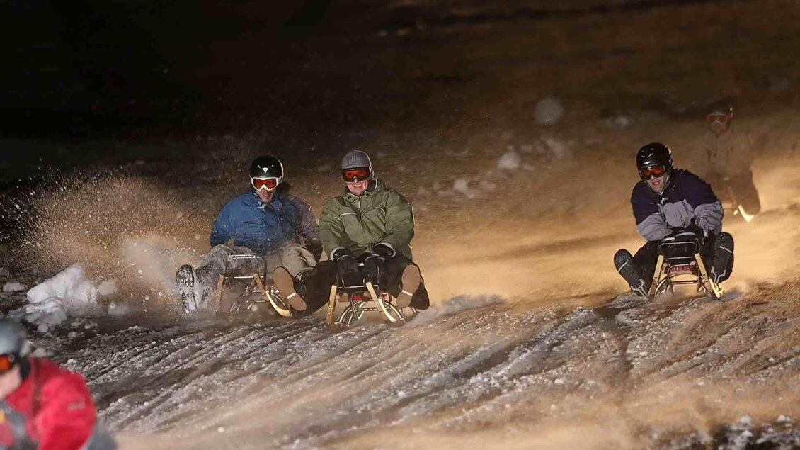 Nachtrodeln auf schneebedeckter Bahn. Spaßige Fahrer gleiten den Hang hinunter.